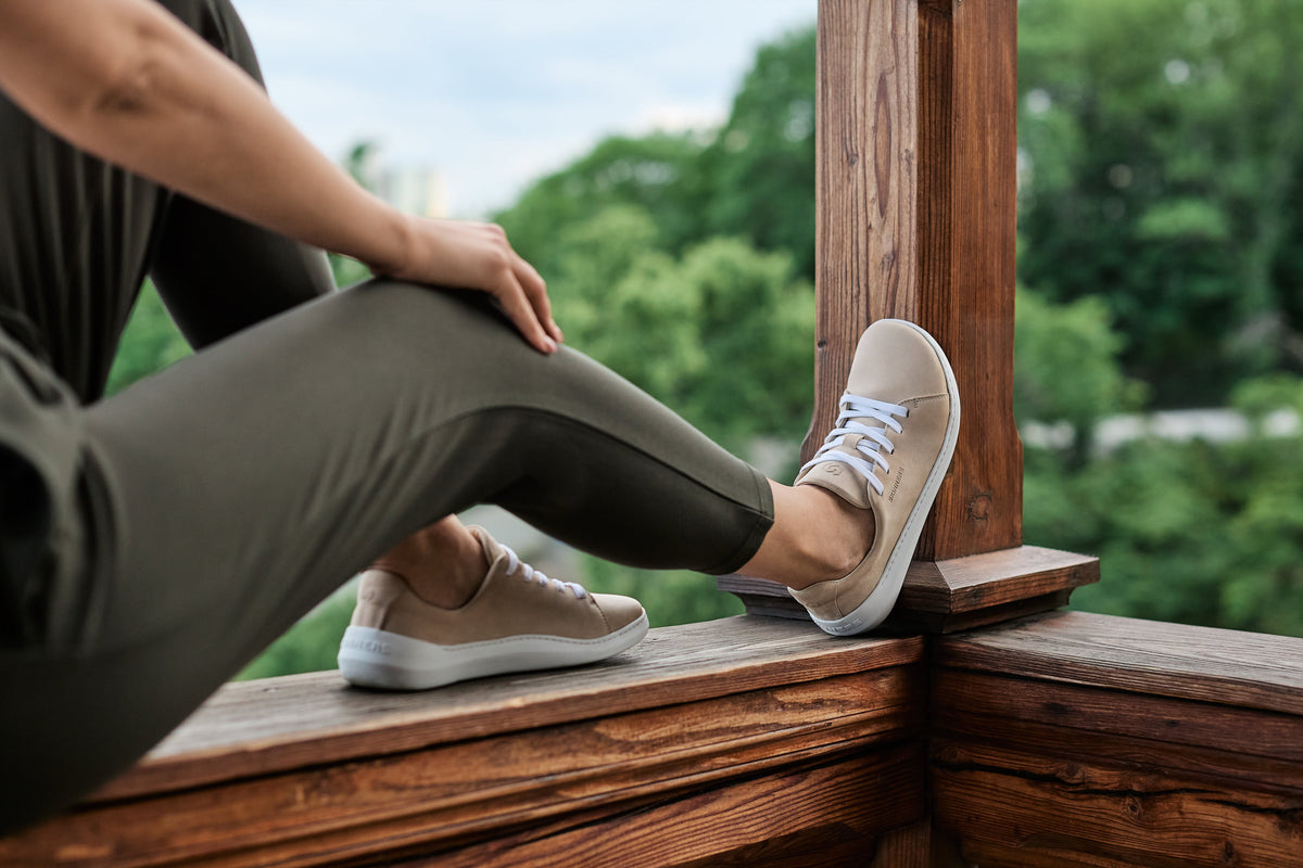 Beige sneakers på fødder ved trægelænder og grønne træer
