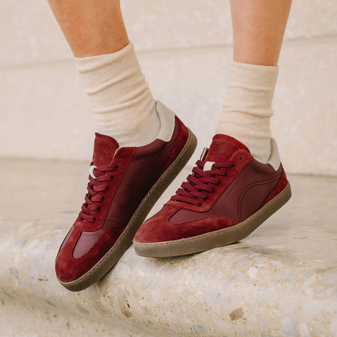 Bordeaux barfodssneakers på fod med lyse sokker på et stentrin