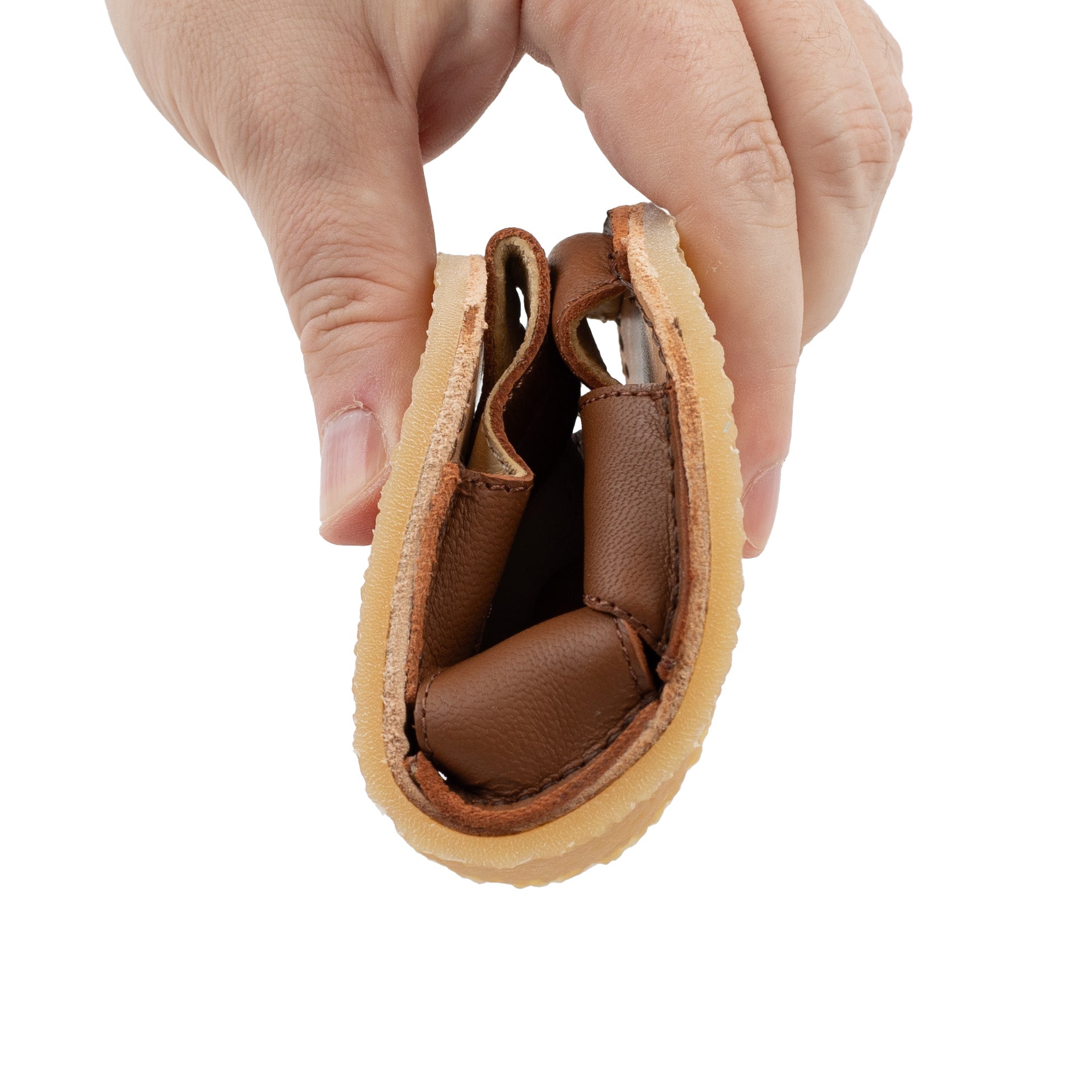 Tikki Lasta Leather sandal Bruno variant for kids in brown leather, shown folded to display flexibility, highlighting barefoot design with a soft, bendable sole.