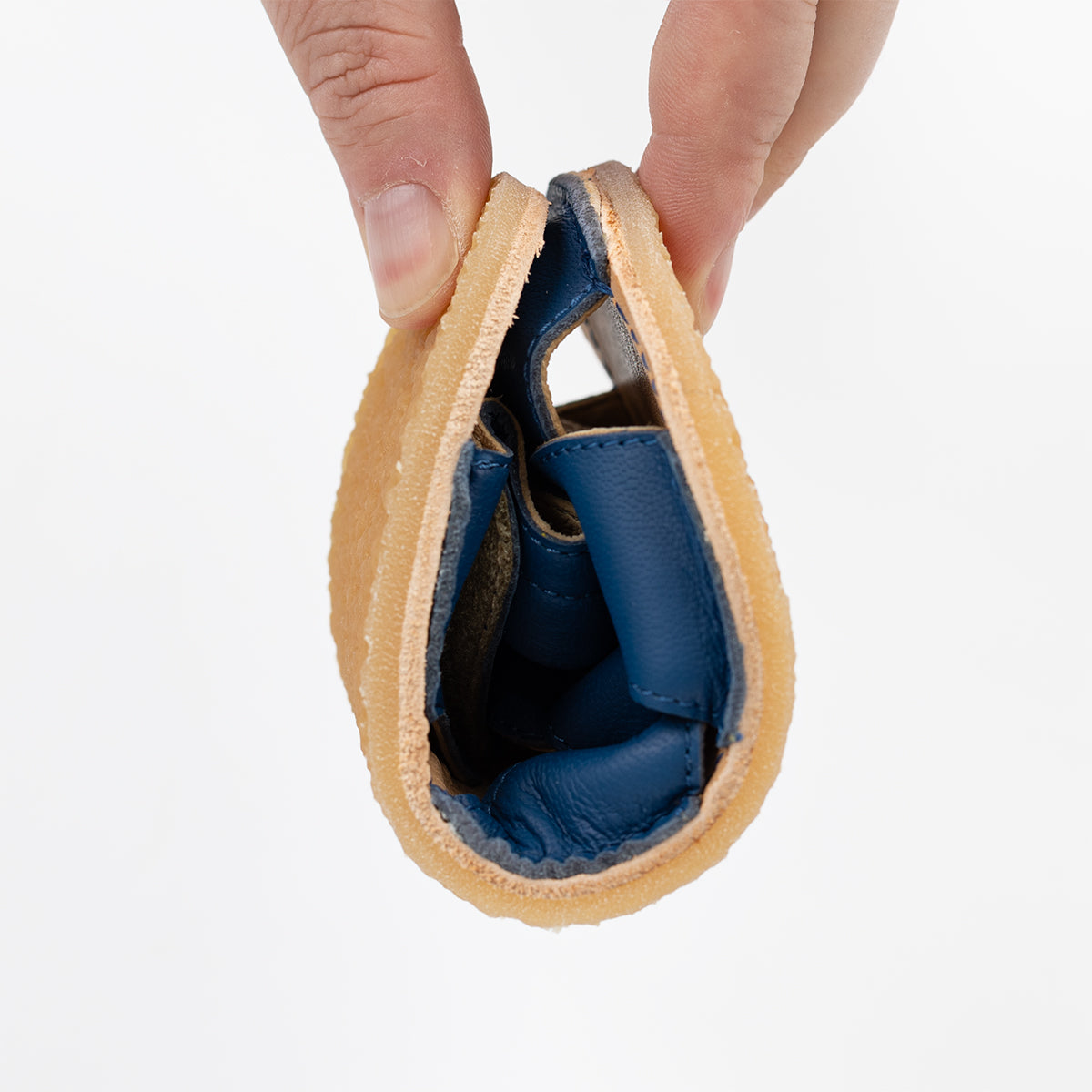 Bøjelig Lasta Leather Mare sandal i blå læder med lysebrun sål, rullet op og holdt af en hånd, som viser dens fleksibilitet. Ideel til børn, der går barfodet.