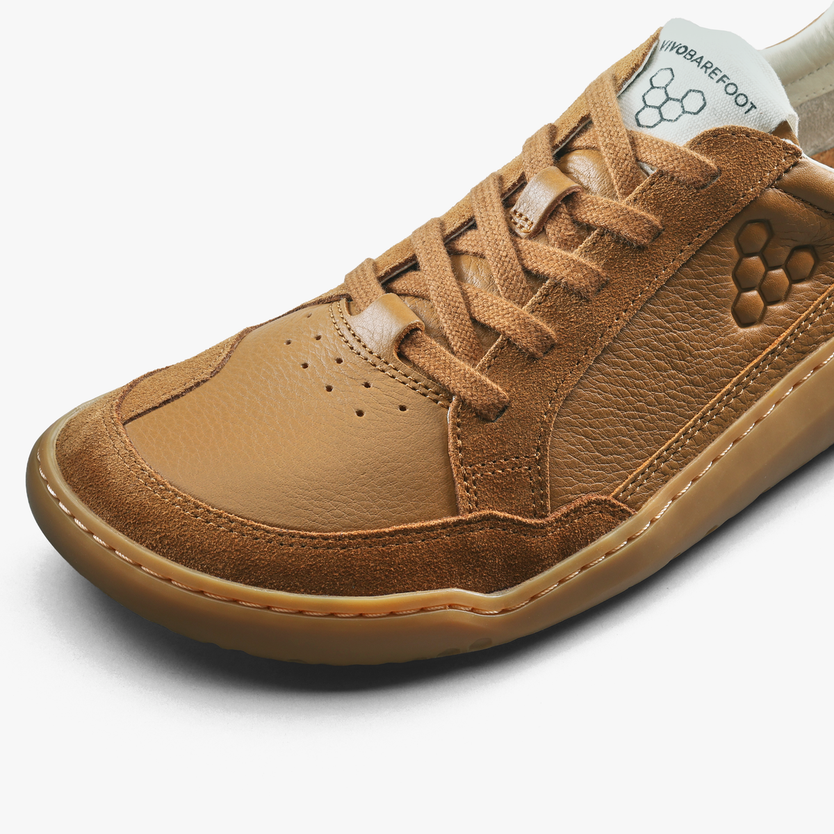 Nærbillede af snørebånd, perforering og sekskantlogo i relief på tan sneaker