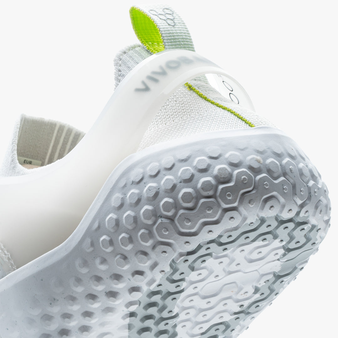 Vivobarefoot Motus Strength Womens i varianten Bright White / Grey, viser hælen og siden. Skoen har en barfods design med hexagonalt mønster på sålen og grønne detaljer.