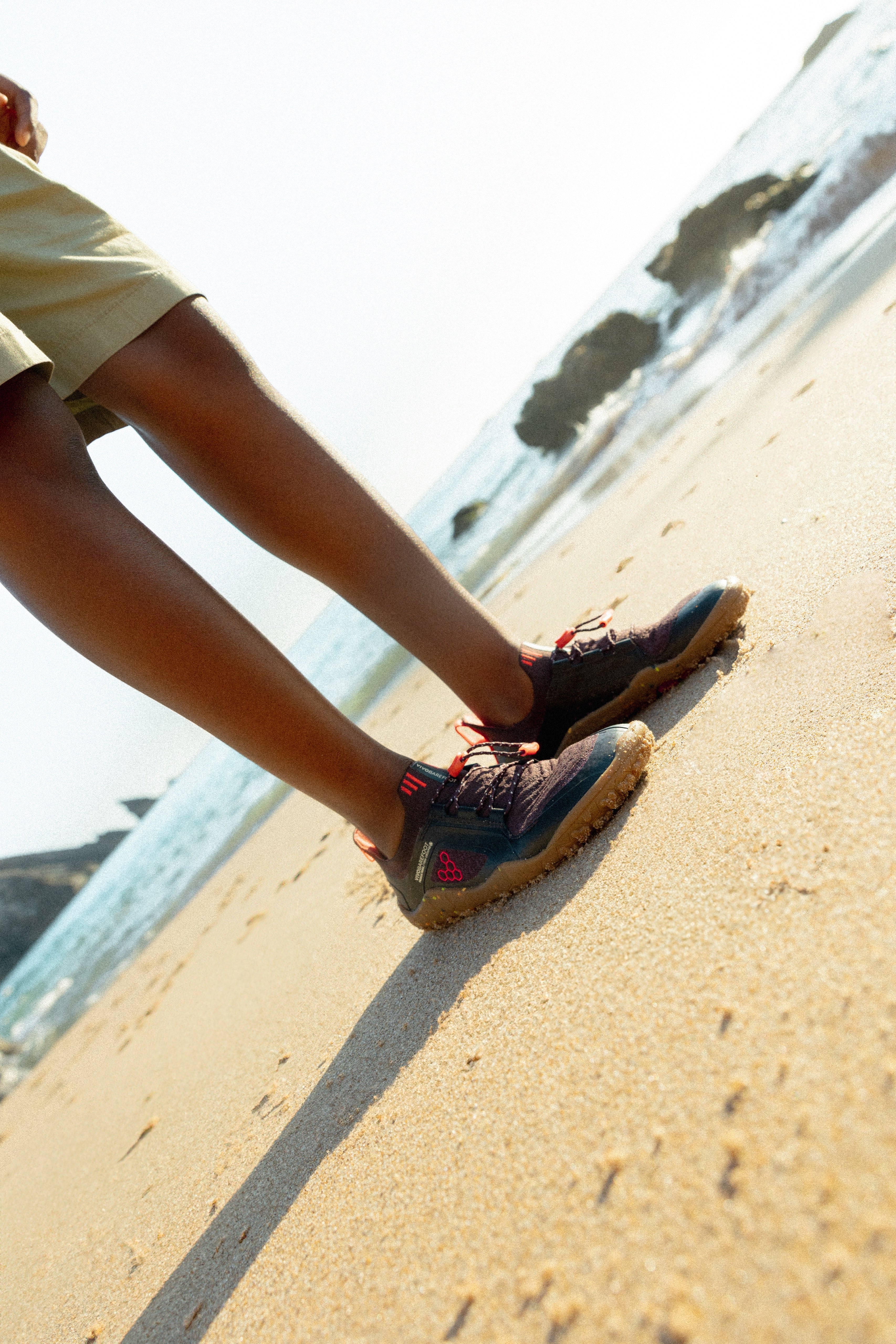 Vivobarefoot Primus Trail Knit FG Juniors barfodssko til børn i farven huckleberry/ molten lava på stranden