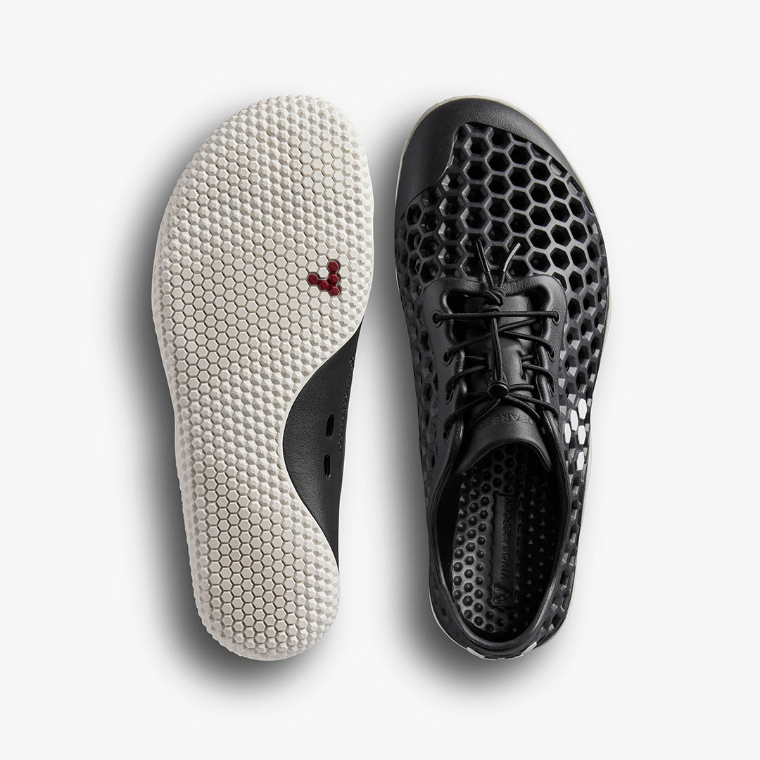 Vivobarefoot Ultra IV Womens sneakers in Obsidian, shown with a white hexagon-patterned barefoot sole and black honeycomb perforated upper with laces.