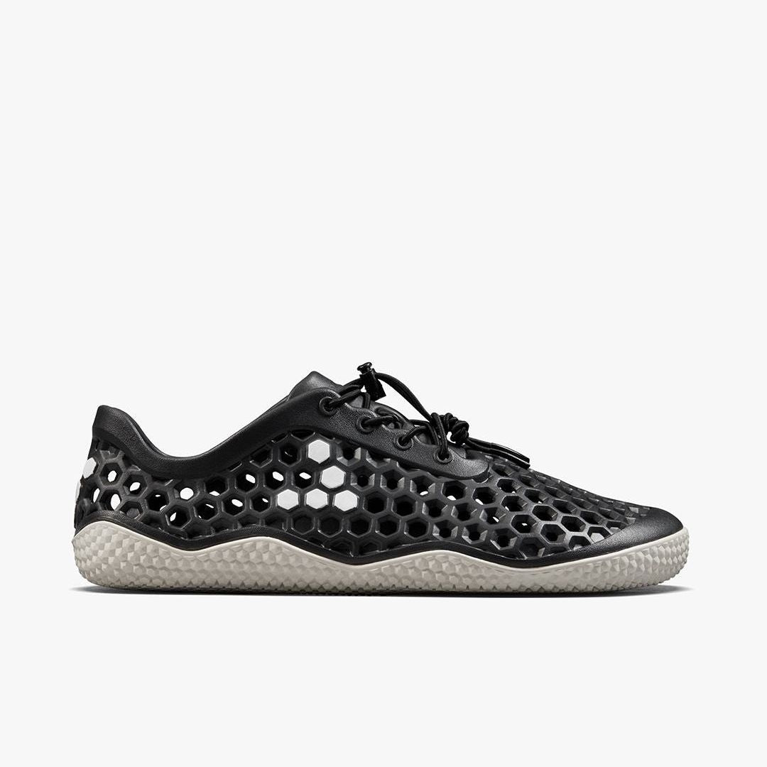 Vivobarefoot Ultra IV Womens sneaker in Obsidian, shown from the side. Black honeycomb upper with breathable cutouts and a light, textured sole. Minimalist, barefoot design.