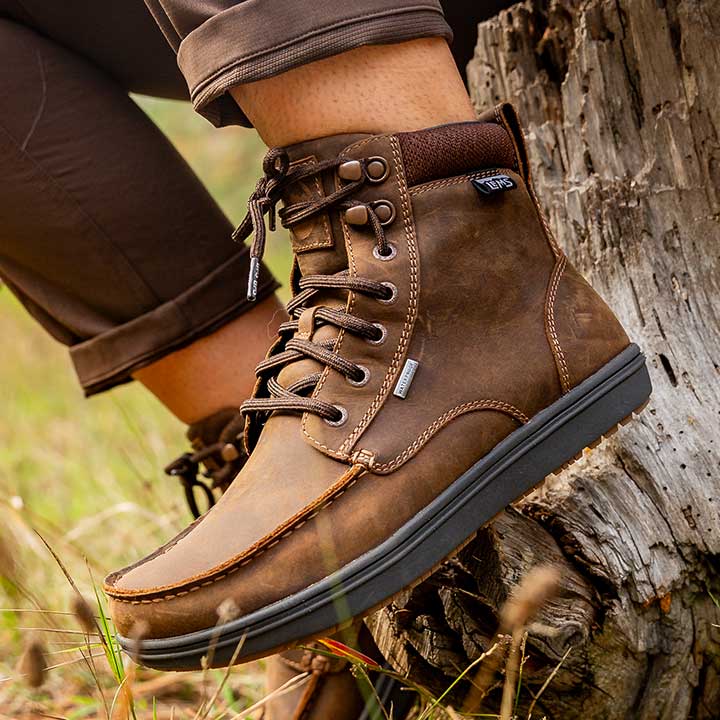 Lems Boulder Boot Grip Waterproof Dakota variant i brun læder, bæres af en person udendørs. Skoen har en robust snørebåndsdesign, polstret krave og synligt logo.