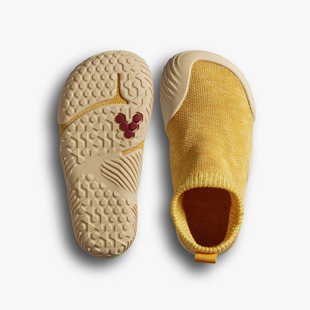 Vivobarefoot Pluma Knit Toddlers i varianten Honey Gold, viser sålen med bikube mønster og rød detalje, samt åndbar strikket overdel i terrakotta. Barfodssko til småbørn.