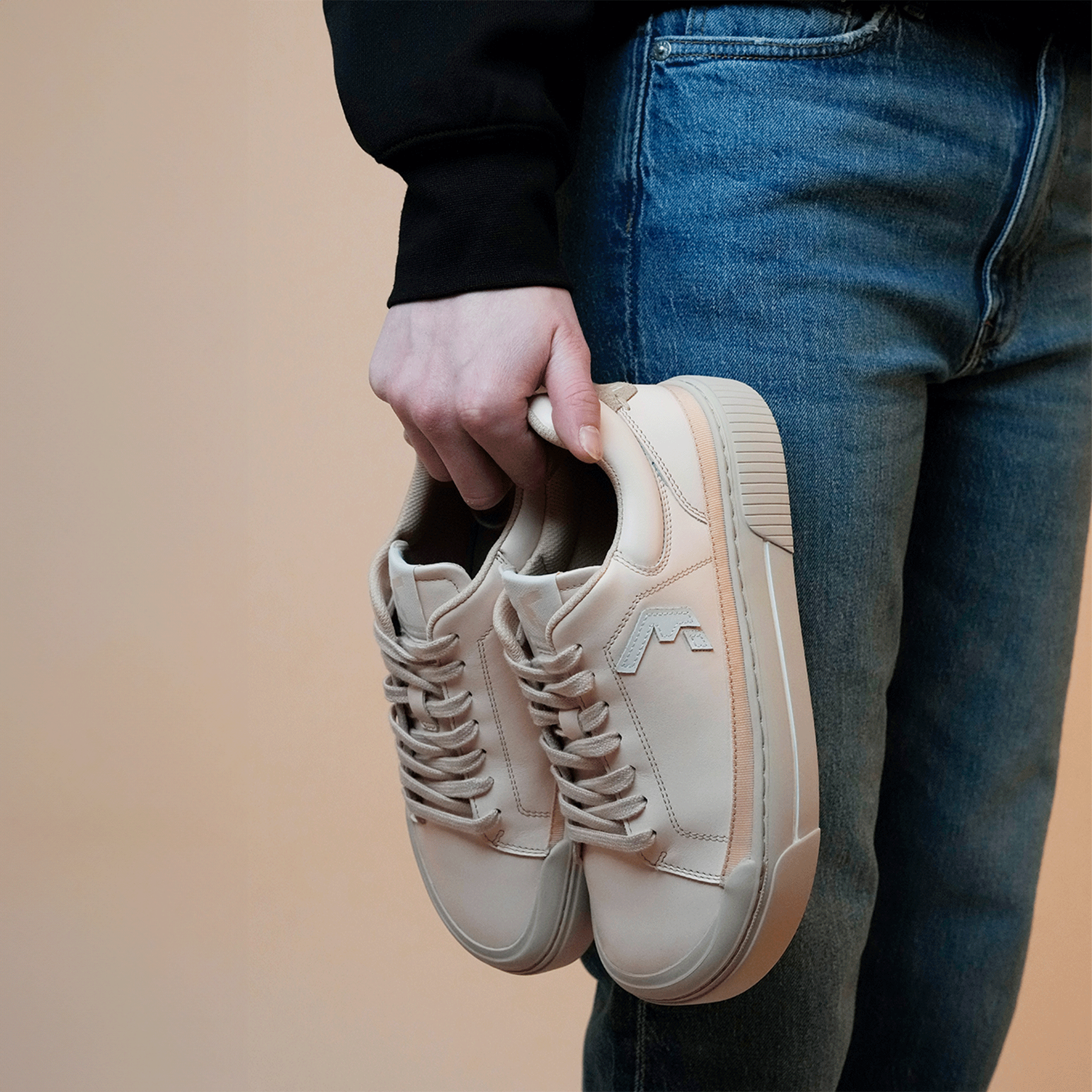 Wyde Arcus sneakers i varianten Peach holdt af en person i jeans og sort trøje. Glat læderfinish med Wyde-logo på siden og tekstureret sål til greb.